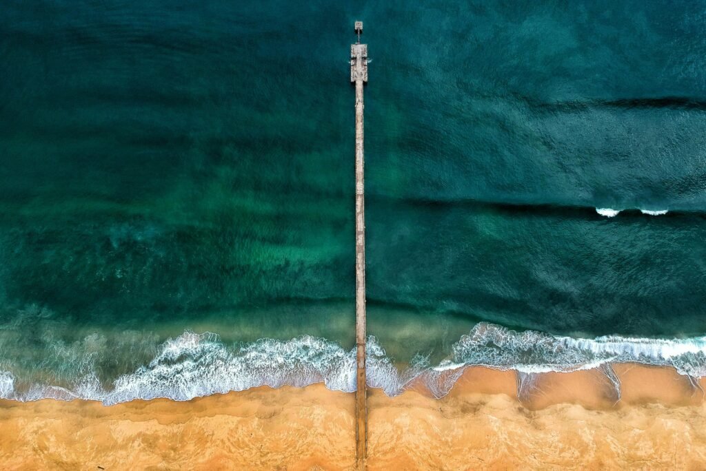 Aerial view of coastal pier with turquoise ocean waters and sandy beach