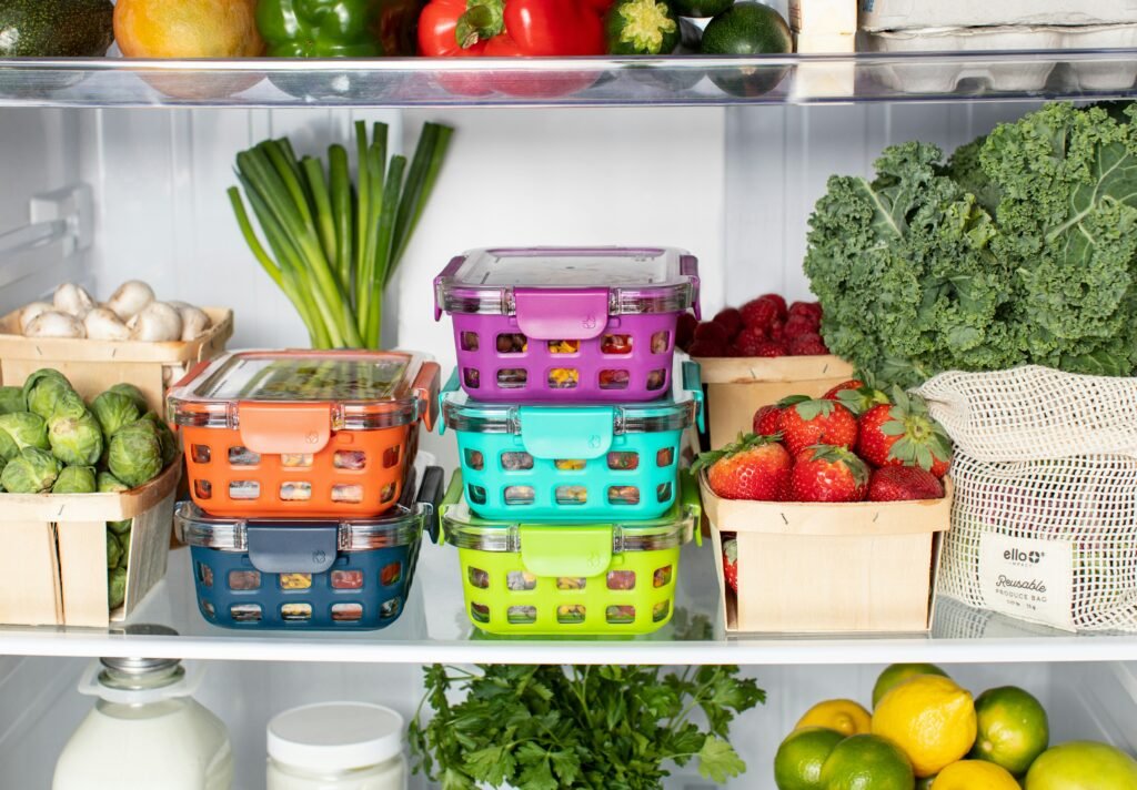 A refrigerator filled with fresh produce, leafy greens, and colorful airtight containers.