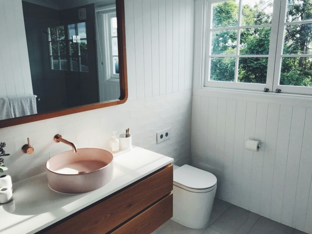 A minimalist bathroom with a wooden vanity, pink sink, and large windows showcasing natural light, promoting a zero-waste lifestyle.