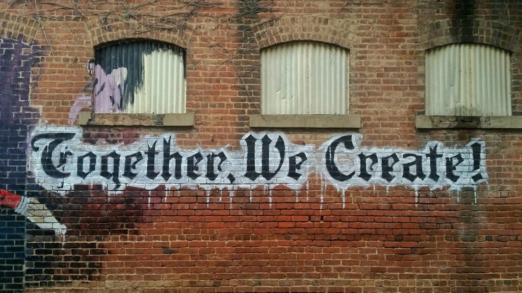 A wall mural with the text 'Together We Create' painted on a brick wall.