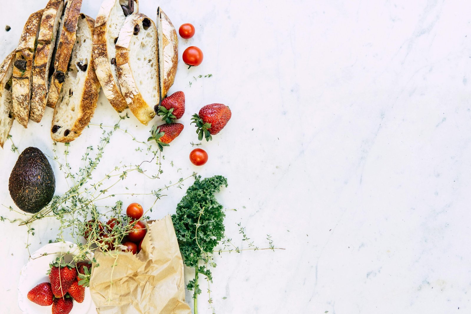 Fresh produce, bread, and herbs on marble counter showing food waste prevention methods