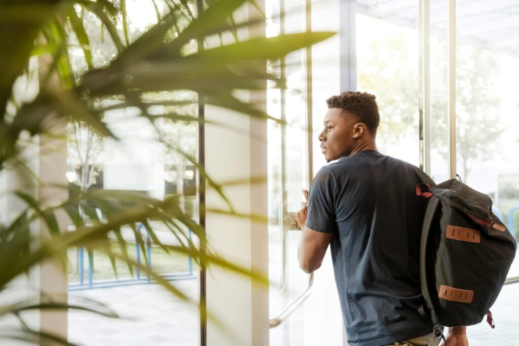 College student with a backpack walking through a bright, plant-filled campus building.