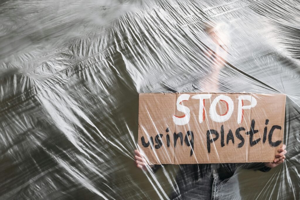 A person holding a cardboard sign that says 'Stop Using Plastic,' behind a plastic sheet.