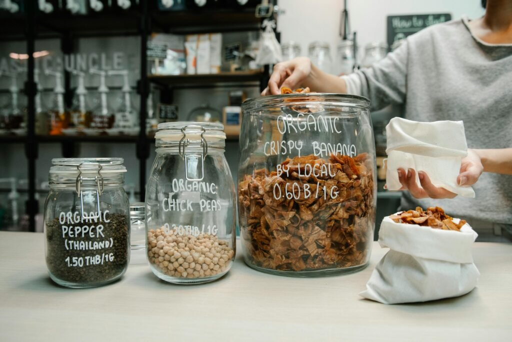 Glass jars filled with organic chickpeas, pepper, and crispy banana chips at a zero-waste store.