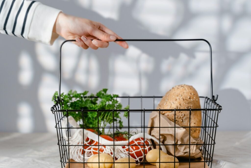 A wire basket with fresh produce, bread, and herbs stored in reusable and plastic-free packaging.